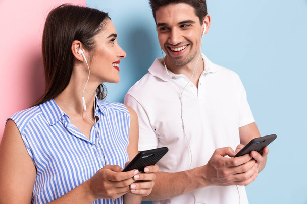 Image of optimistic man and woman wearing earphones and using smartphones isolated over colorful background - Foto, Imagem