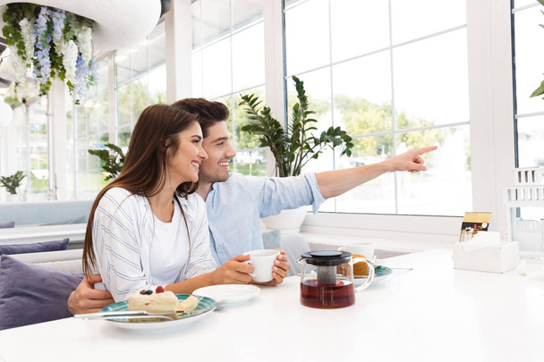 Image étonnante jeune couple amoureux assis dans le café manger des desserts et boire du thé regardant de côté pointant
. - Photo, image