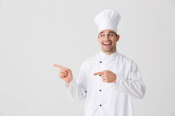Image of handsome excited young man chef indoors isolated over white wall background pointing. - Фото, изображение