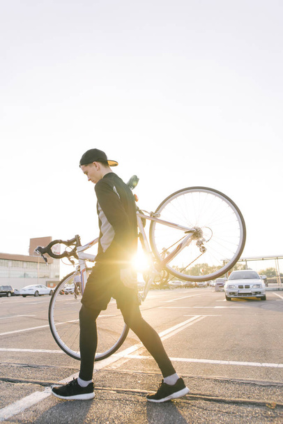 Молода людина є велосипедист в темних спортивний одяг, несучи шосе велосипед на його плечі, на тлі заходу сонця. Райдер тягне велосипед на спині - Фото, зображення