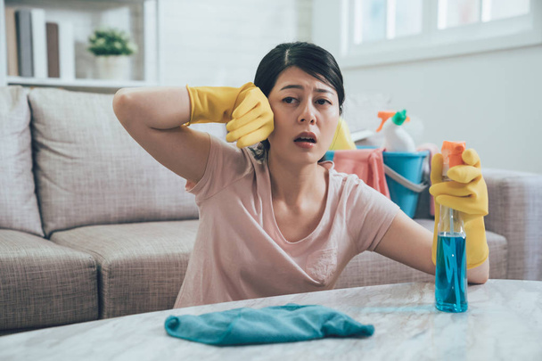 asian woman using sprayer and rag wiping table. young housewife feeling tired wipe sweat by hands in protective gloves. elegant housekeeper doing her house chores. - Φωτογραφία, εικόνα