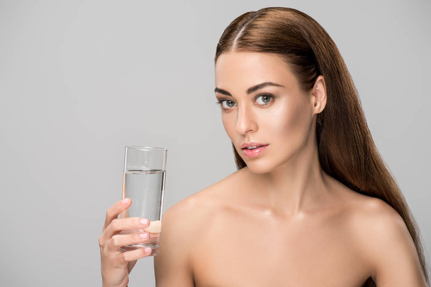 schöne brünette nackte Frau hält Glas Wasser isoliert auf grau - Foto, Bild