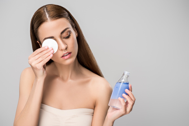 attractive girl removing makeup with cotton disk and skincare product, isolated on grey - Fotografie, Obrázek