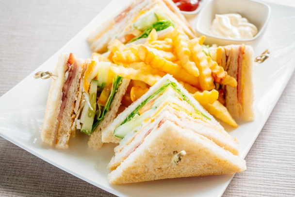 Клубный сэндвич с сыром и ветчиной и соусом в белой тарелке
 - Фото, изображение