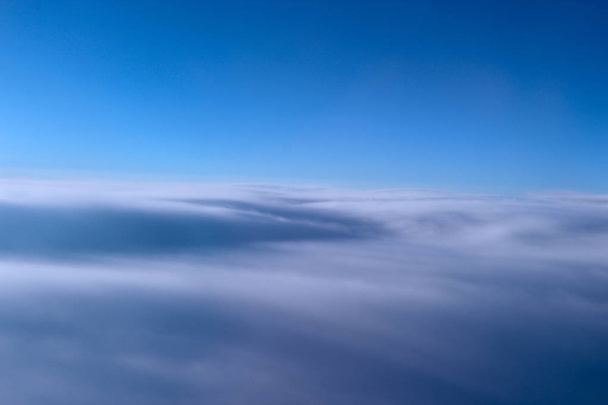 Красивая панорама из окна самолета на утреннем солнце над облаками. Необычные облака, освещенные лучами солнца. Красивые белые облака на голубом фоне неба. Пейзаж с солнцем и небом. Панорама неба
 - Фото, изображение