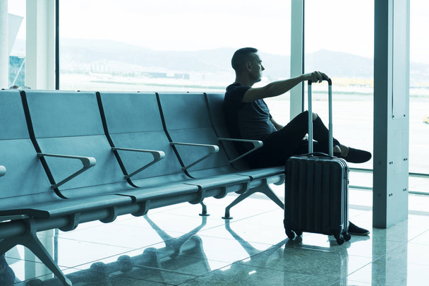 un jeune homme caucasien, avec son chariot, attendant son vol assis dans la salle d'attente d'un aéroport
 - Photo, image