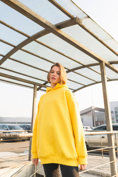 Sokakta duran ve kameraya poz bir sarı hoodie büyüleyici bir kız moda portre. Lookbook. Sokak moda portre - Fotoğraf, Görsel