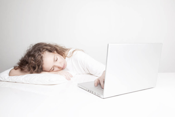 túlhajszolt vöröshajú nő alszik a munkahelyen, miközben dolgozik a laptop előtt fehér fal  - Fotó, kép