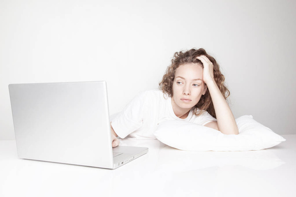 aborrecido jovem mulher trabalhando com laptop na frente da parede branca
  - Foto, Imagem