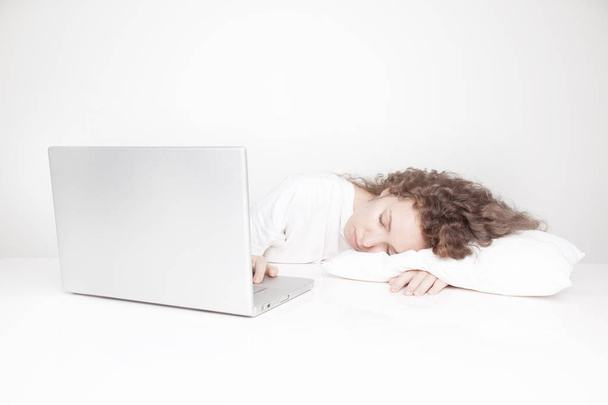 Müde rothaarige Frau schläft am Arbeitsplatz, während sie mit Laptop vor weißer Wand arbeitet  - Foto, Bild