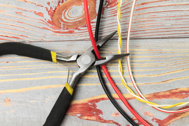 Cutting cable with pliers, on a wooden background in the old style, there is toning, close-up - Foto, immagini