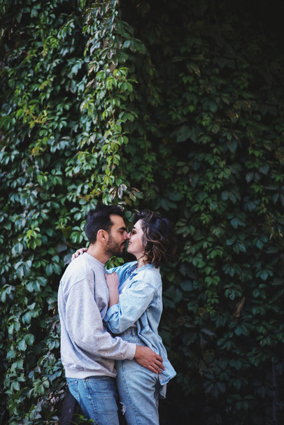 Beautiful couple hugging and kissing against the background of the green leaf wall. - Фото, изображение