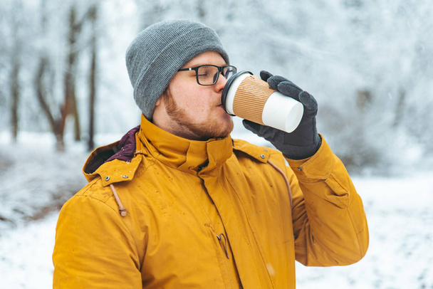 portrét silné usmívajícího se muže pití kávy v zasněžované městský park koncept - Fotografie, Obrázek