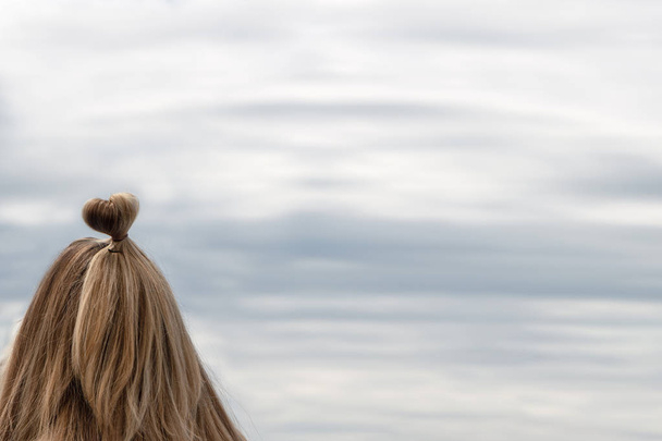 Meisje met kapsel in de vorm van een hart op de achtergrond van de zee, de hemel - Foto, afbeelding