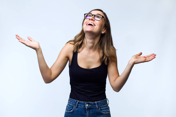 Shot of beautiful laughing young woman with eyeglasses looking to the roof over white background. - Zdjęcie, obraz