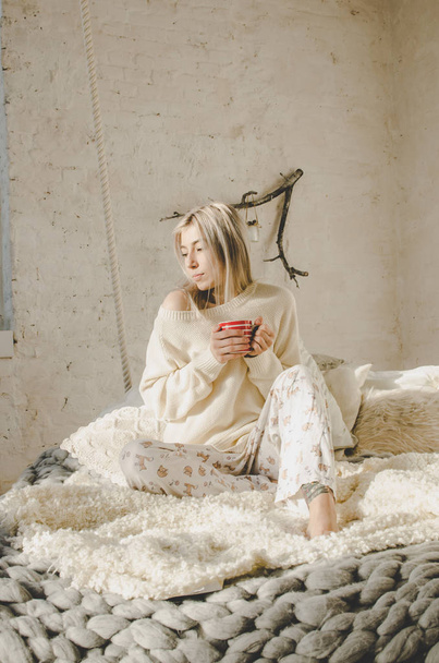 beautiful blonde young woman sitting on bed and holding cup of drink - Φωτογραφία, εικόνα