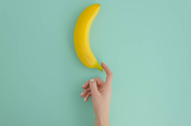 Flat lay female hand and banana on mint background. Fruit concept. Mock up. Top view. Copy space. - Foto, Imagen