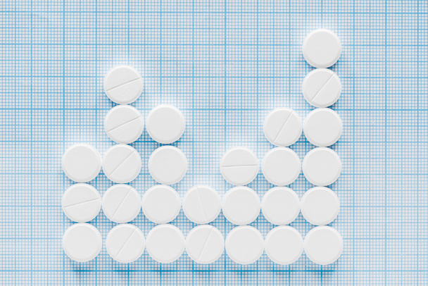 verhoogde weergave van gearrangeerde witte pillen op blauwe geruite oppervlak - Foto, afbeelding
