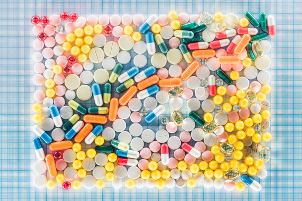 leigos planos com retângulo feito de várias pílulas coloridas na superfície quadriculada azul
 - Foto, Imagem