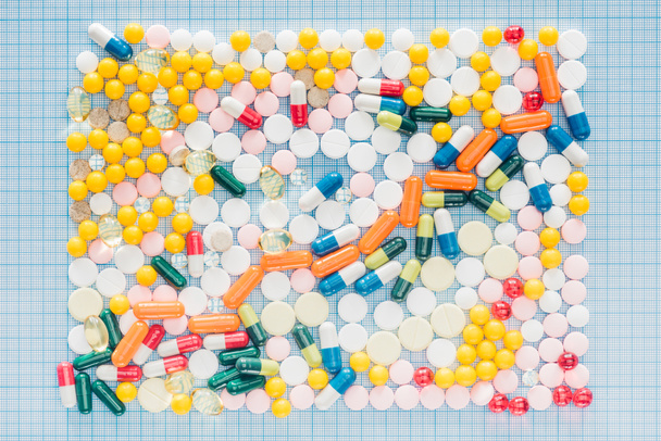 vista superior del rectángulo hecho de varias píldoras de colores en la superficie a cuadros azul
 - Foto, imagen