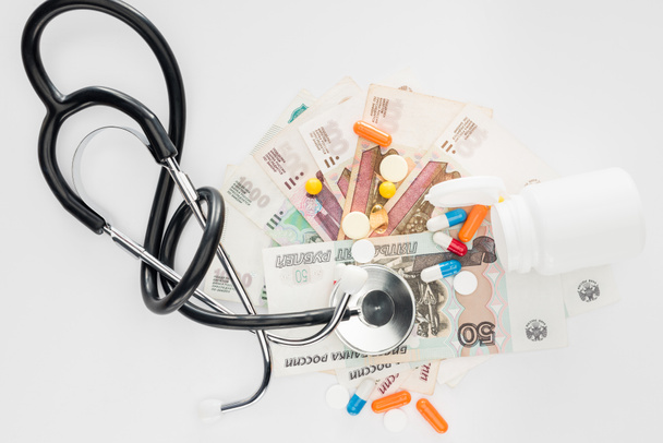 verhoogde weergave van stethoscoop, kleurrijke verschillende pillen en Russische bankbiljetten op witte ondergrond - Foto, afbeelding