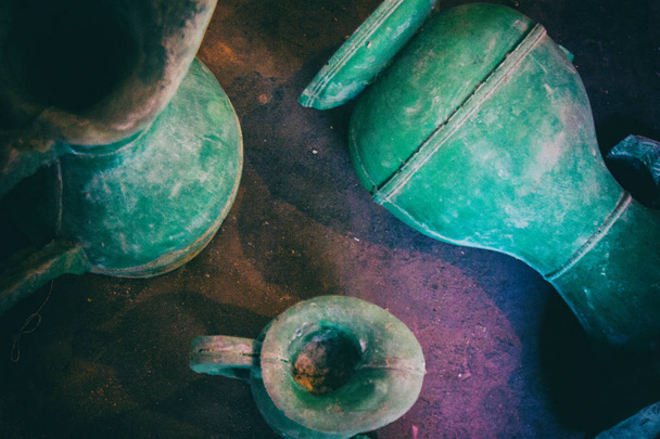Behang achtergrond van oude vintage versleten groene keramische water vazen op de vloer in de buurt van een raam met daglicht van de buitenkant. Geen mensen.. - Foto, afbeelding