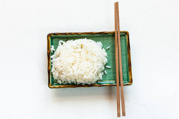 вид сверху на порцию вареного риса и палочек для еды на зеленой пластине на белой бетонной доске с копирайтом
 - Фото, изображение