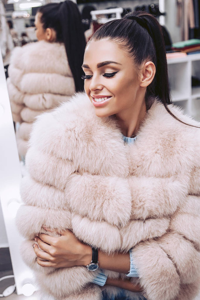 A cute brunette dressed in a pink fur vest in a clothing store - Photo, Image