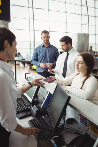 Mulher que dá o passaporte ao acompanhante de check-in da companhia aérea no balcão de check-in do aeroporto
 - Foto, Imagem