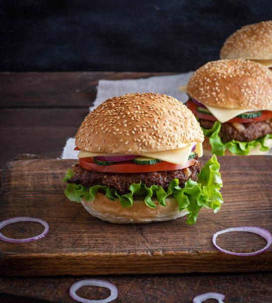 cheeseburger with meat patties and white sesame bun on a brown wooden table - Фото, изображение
