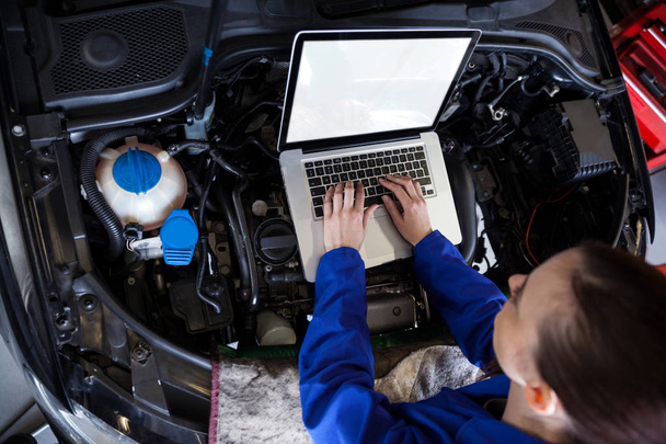 女性メカニック修理ガレージで車のエンジンを処理しながらデジタル タブレットを使用して - 写真・画像