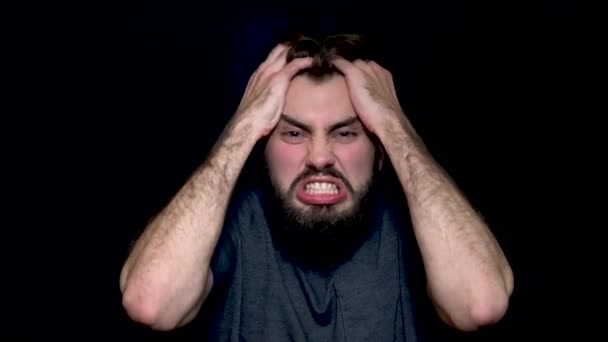 Angry young man shouting, expressing negative emotions, tearing his hair out, isolated on black background. Close up of a stressed young man shouting and screaming - Footage, Video