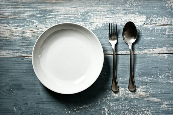 empty dish with fork and spoon on blue table - vintage effect - closeup - Foto, afbeelding