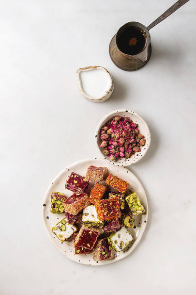 Variety of traditional turkish dessert Turkish Delight with rose petals and pistachio nuts on ceramic plate with coffee jezve and milk jug over grey spotted background. Flat lay, space - Фото, зображення