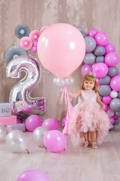 Princess baby girl celebrating life event wearing golden crown and pink airy dress. Cute girl posing in pastel colors studio shoot with air baloons and cake - Foto, Imagem