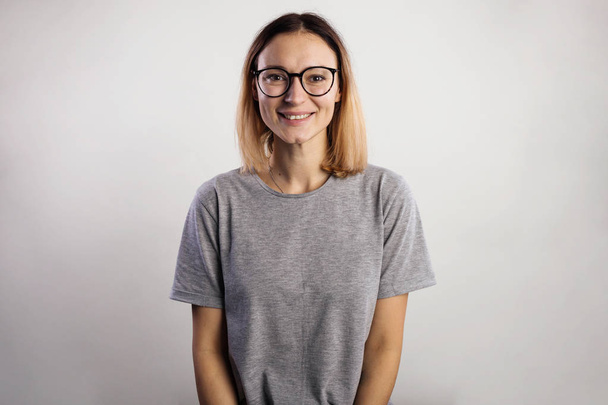 Portrait of a casual woman in big glasses and gray shirt looking at camera isolated on a gray background - Foto, immagini