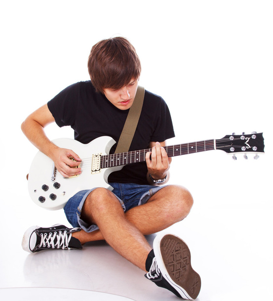Панк-підліток грає на гітарі, сидячи на підлозі
 - Фото, зображення