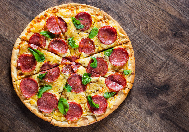 Pepperoni Pizza with Mozzarella cheese, salami, Tomato sauce, pepper, Spices and Fresh Basil. Italian pizza on wooden table background - Photo, Image