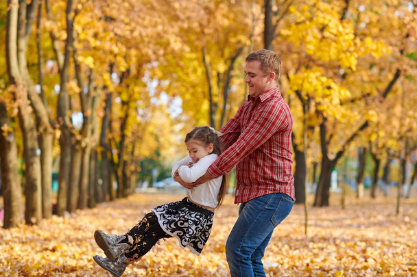 Apa és lánya játék és szórakozás a őszi városi park. Pózol, mosolyog, játszik. Világos sárga fák. - Fotó, kép