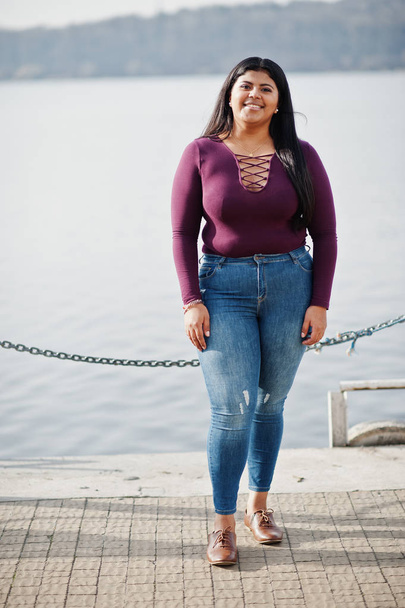 Pretty latino xxl model girl from Ecuador wear on violet blouse posed against lake. - Zdjęcie, obraz