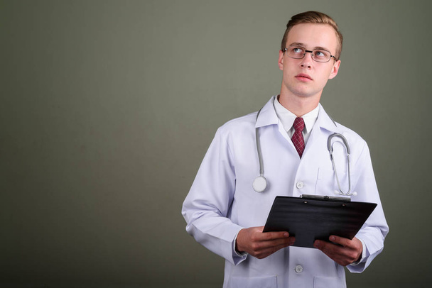 Junger schöner Mann Arzt vor farbigem Hintergrund - Foto, Bild