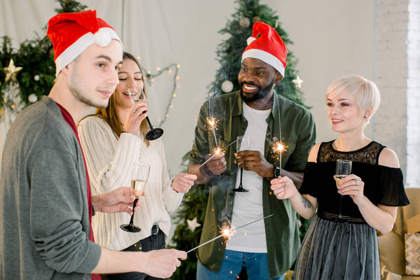 Young african boy and Caucasian girls and boy smiling and celebrating New Year or Christmas with champagne and bengal fires. - Foto, Bild