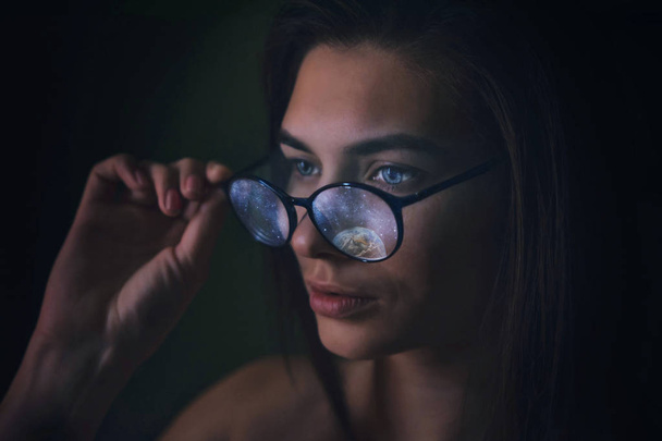 Girl in glasses with the reflection of cosmic stars of the planets, portrait of a woman advertising optics. Unusual Magic Eyeglass Lens - Photo, Image