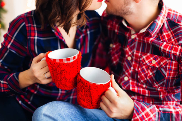 Un gros plan des tasses rouges avec une couverture tricotée rouge qui tiennent le gars et la fille
 - Photo, image
