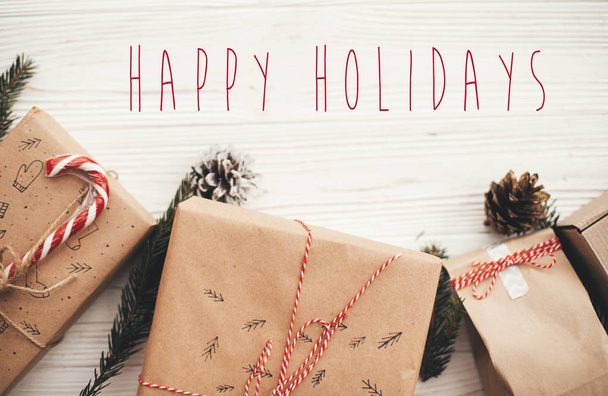 frohe Feiertage Text auf Weihnachten stilvolle Geschenke mit roter Schleife, Zuckerrohr, Tannenzweige und Zapfen. Glückwunschkarte der Saison. Frohe Weihnachten und ein gutes neues Jahr - Foto, Bild