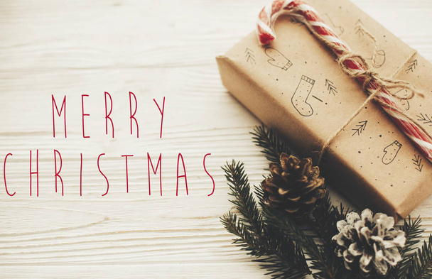 Χαρούμενα Χριστούγεννα κείμενο σε κομψό Χριστούγεννα παρουσιάζει με κόκκινη κορδέλα, από ζαχαροκάλαμο καραμέλα, κλάδους πεύκων και κώνοι. Ευχετήρια κάρτα. Καλές γιορτές και Ευτυχισμένο το νέο έτος - Φωτογραφία, εικόνα