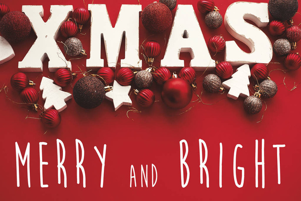 Merry και φωτεινά Χριστούγεννα κείμενο σε ξύλινη λέξη Χριστούγεννα με κόκκινα στολίδια σε ρουστίκ άσπρο φόντο, επίπεδη θέσει. Ευχετήρια κάρτα. Καλές γιορτές και Ευτυχισμένο το νέο έτος - Φωτογραφία, εικόνα