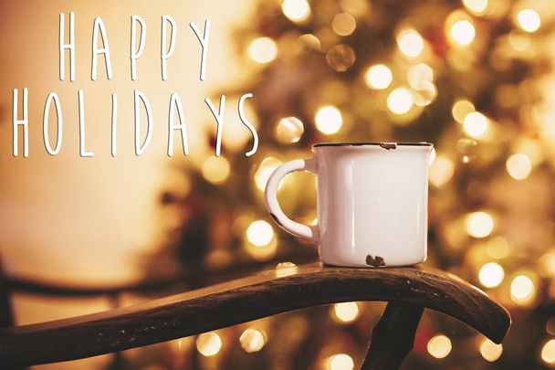 Щасливі свята текст на кружки з гарячим напоєм на старий дерев'яний стілець на Золотий Різдвяні вогні дерева у святковий зал. Вітальна картка. З новим роком та Різдвом - Фото, зображення