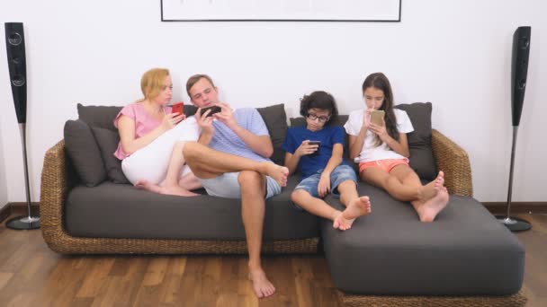 Charming family, mom, dad, daughter and son are watching TV in the living room together, everyone is looking into his phone - 映像、動画