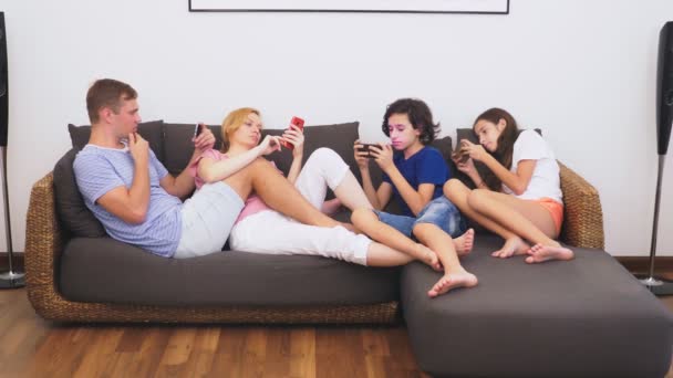 Charming family, mom, dad, daughter and son are watching TV in the living room together, everyone is looking into his phone - Πλάνα, βίντεο